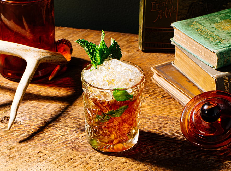 Botanical Julep cocktail in a tumbler on a desk with books and antlers