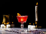 PF Negroni cocktail in a martini glass in front of a line of candles